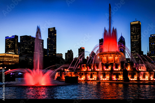 фотография Buckingham Water fountain in red as the twilight sky turns purple silhouetting the Chicago city skyline