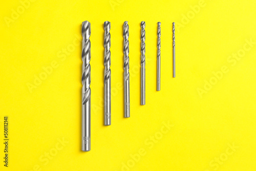 Different drill bits on yellow background  flat lay