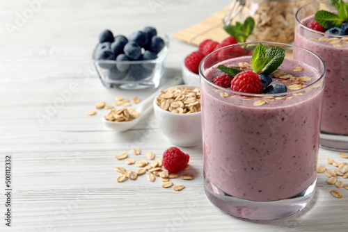 Tasty smoothie with berries, mint and oatmeal on white wooden table, space for text