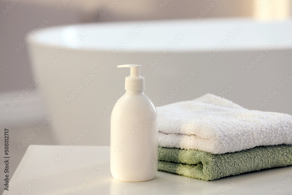 Bottle of bubble bath and towels on white table in bathroom, space for text Bottle of bubble bath and towels on white table in bathroom, space for text