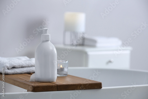 Bottle of bubble bath with foam  towel and candle on tub in bathroom  space for text