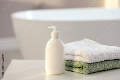 Bottle of bubble bath and towels on white table in bathroom, space for text