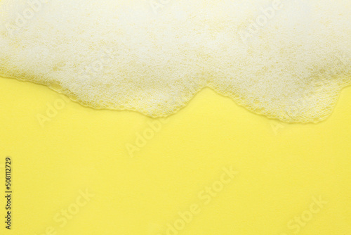 Fluffy bath foam on yellow background, top view. Space for text