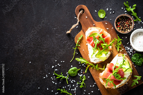 Open sandwich with cream cheese and prosciutto or jamon with fresh greens. Top view at dark.
