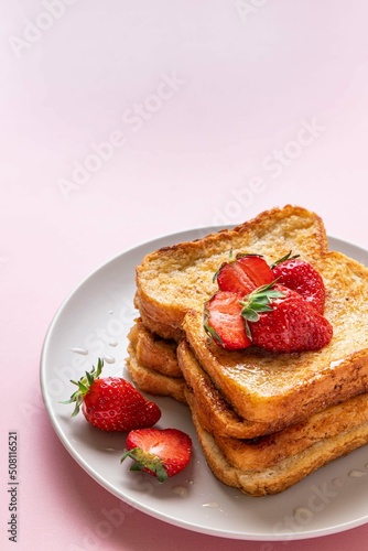 Traditional french toasts with strawberries and honey on pink background. Summer breakfast, brunch or lunch with berries. Copy space. Selective focus.