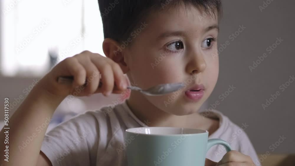 Hungry little boy leaning on the kitchen table at home and eating ice cream from cup. Delicious breakfast. Hungry little boy leaning on the kitchen table at home and eating ice cream from cup. Delicious breakfast.