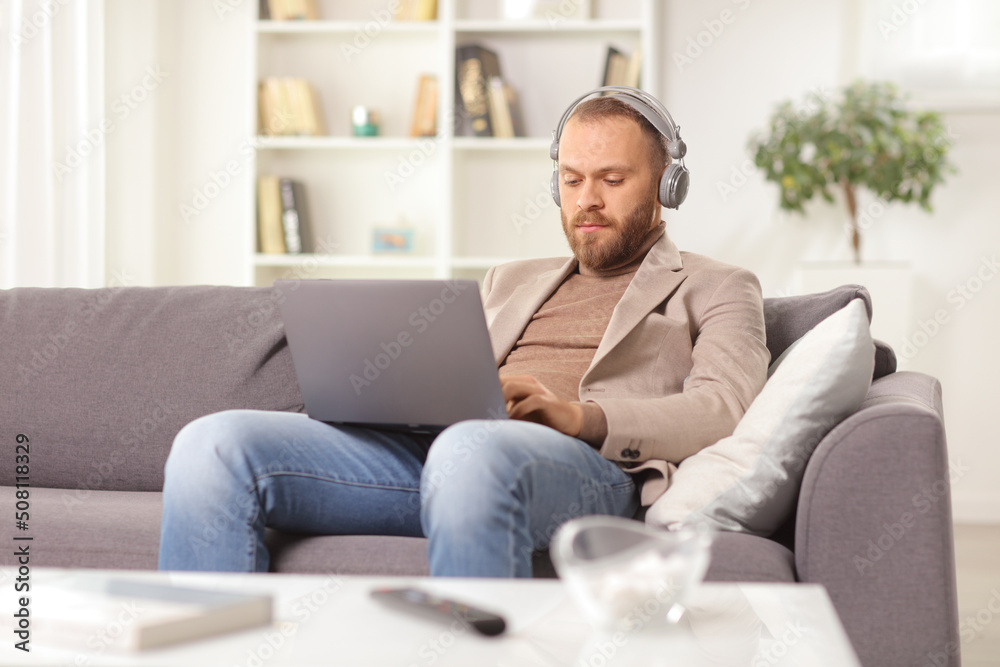 Man with headphones using a laptop and sitting on a sofa Man with headphones using a laptop and sitting on a sofa
