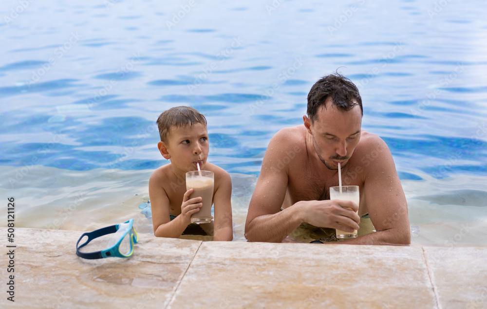 Father and son in the pool drinking milkshakes. International Father's Day concept Father and son in the pool drinking milkshakes. International Father's Day concept