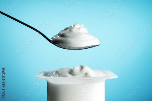 White plastic pot with yogurt and spoon on blue background photo