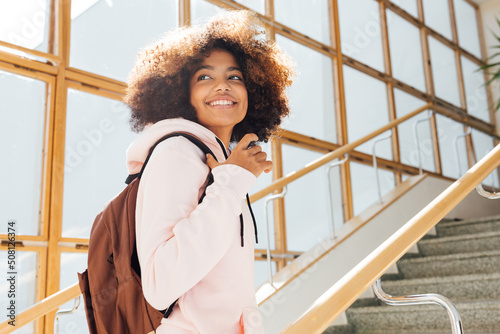 Smiling girl looking back while standing on stairs in school. Student going for the lecture.