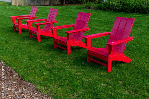 Row of red Adirondack chairs at lake shore on a grassy lawn © Focused Adventures