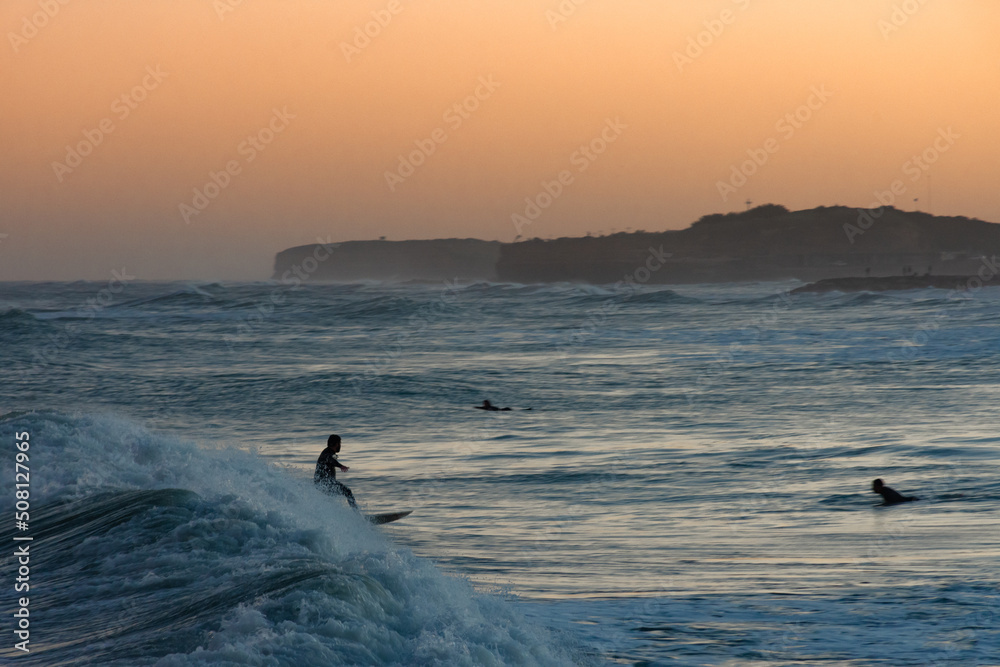 Fototapeta premium Man surfing a wave at orange sunset