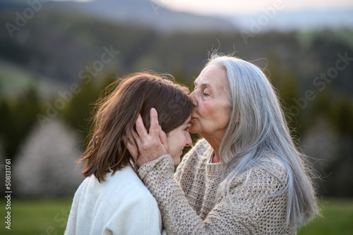 Obraz na plátně Happy senior grandmother kissing her teenage granddaguhter on forehead in nature on spring day