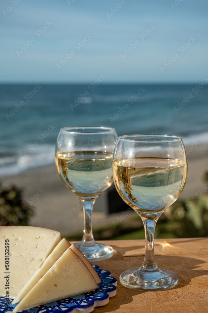 Spanish hard manchego, cow, sheep and goat cheese served outdoor with glasses of white wine and view on blue sea Spanish hard manchego, cow, sheep and goat cheese served outdoor with glasses of white wine and view on blue sea