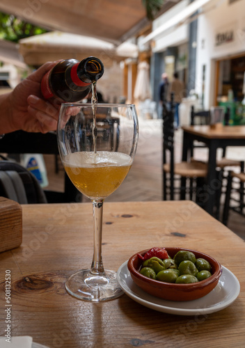 Pouring of beer from bottle in Spanish outdoor cafe, tapas bowl with green olives © barmalini