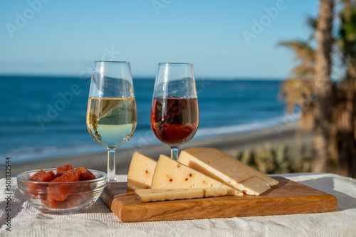 Spanish hard Andalusian cheese filled with sweet sherry served outdoor with membrillo jam with two glasses of sherry wine with beach and blue sea on background