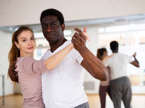 Young smiling woman learning to dance waltz paired with african american man in dancing class..