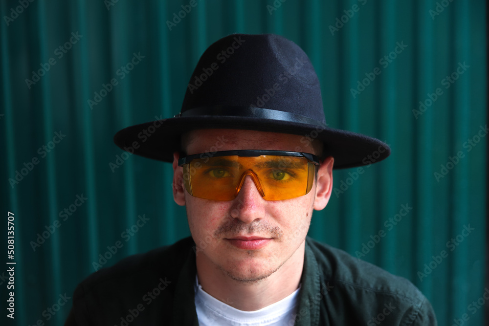 Happy fashion man. Portrait of handsome smiling stylish hipster lambersexual model. Man dressed in yellow sunglasses and black hat. Fashion male on the modern background. Caucasian