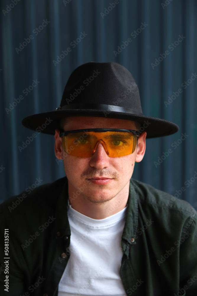 Happy fashion man. Portrait of handsome smiling stylish hipster lambersexual model. Man dressed in yellow sunglasses and black hat. Fashion male on the modern background. Caucasian. Guy Happy fashion man. Portrait of handsome smiling stylish hipster lambersexual model. Man dressed in yellow sunglasses and black hat. Fashion male on the modern background. Caucasian. Guy