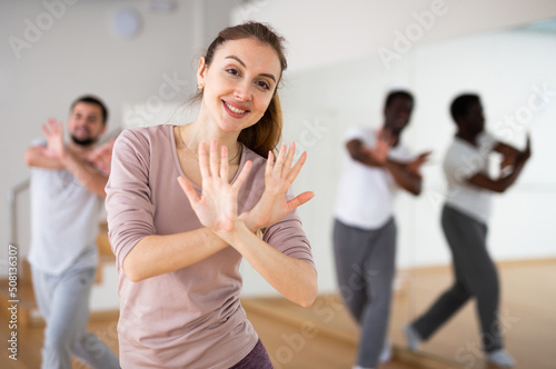 Cheerful woman dancing aerobic dance to warm up during group fitness training in studio.