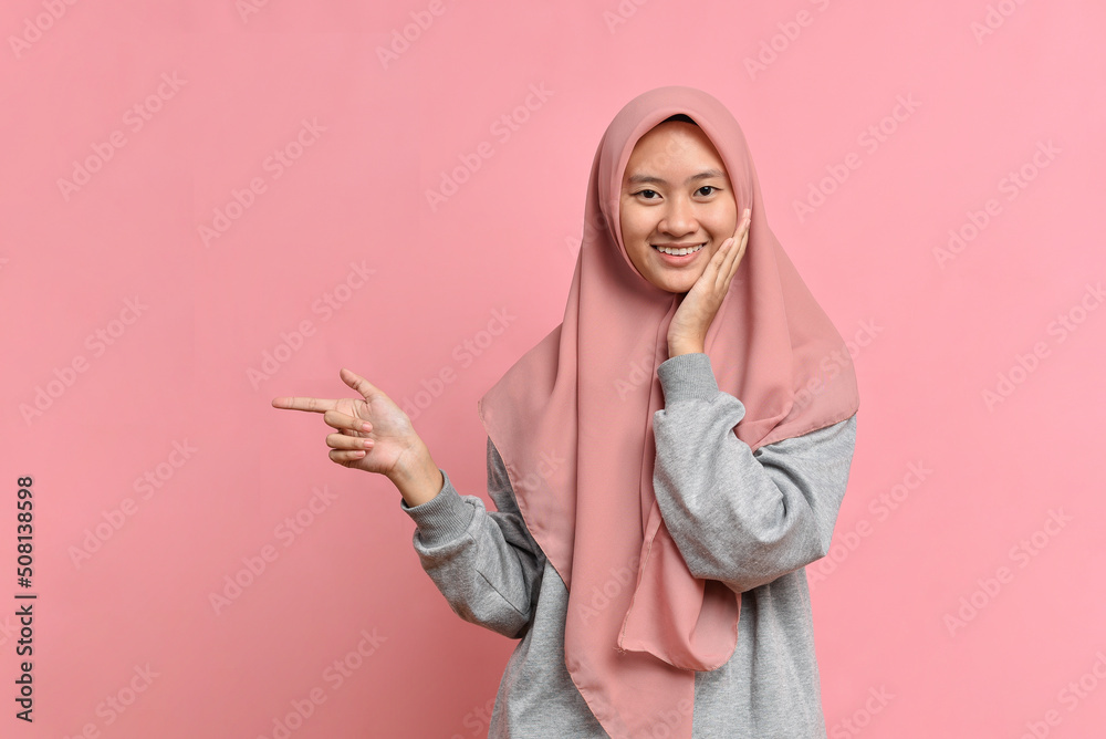Portrait of smiling musllim woman pointing away and looking at the camera Portrait of smiling musllim woman pointing away and looking at the camera