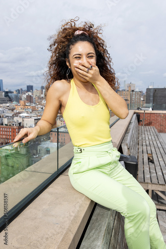 Pretty African American woman with curly hair outside on roof with a view of New York City.