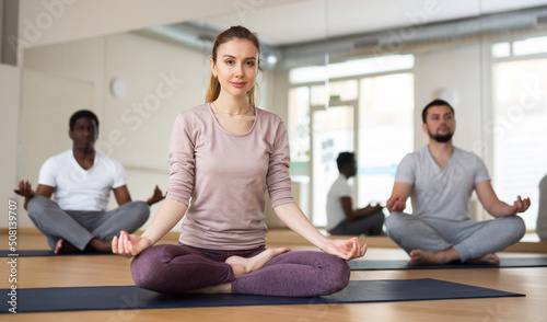Young sporty woman enjoying meditation in modern yoga studio  sitting in lotus position while her hands resting on knees with fingers folded in mudra