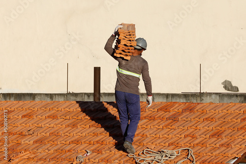 Roofer working on roofing construction. Bricklayer roof repair. House under construction. Workman renovates waterproofing roof of building. Carpenter construction worker carry pile of tiles