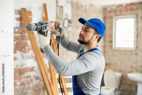 Professional builder working on a construction site during the capital repairs of a house drills a wall with a hammer drill photo