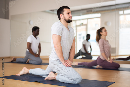 Caucasian man practising stretching asana with people during group yoga training.