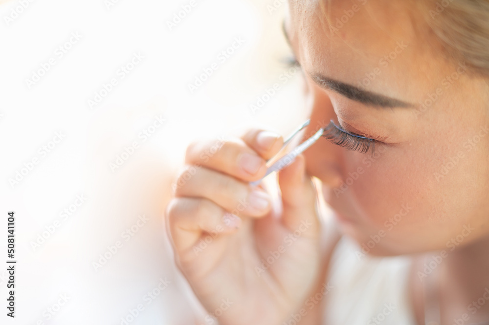 Female hand holding the eyelash and preparing to attach to her eye. Female hand holding the eyelash and preparing to attach to her eye.