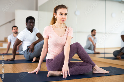 Woman practising lord of the fishes pose with two men during yoga training.