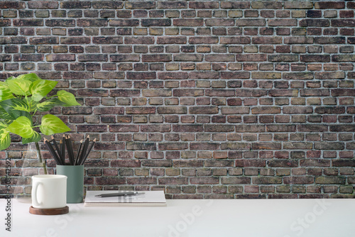 Coffee cup, houseplant and pencil holder on white table against brick wall. Copy space for your text.