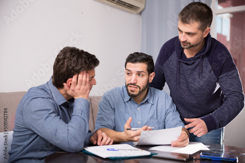 Three men having problems with some documents, worriedly discussing at home.