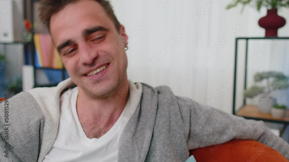 Close up of handsome happy young caucasian winner lucky man smiling friendly, glad expression looking away dreaming resting, relaxation, feel satisfied concept, good news sitting on sofa at home room Close up of handsome happy young caucasian winner lucky man smiling friendly, glad expression looking away dreaming resting, relaxation, feel satisfied concept, good news sitting on sofa at home room