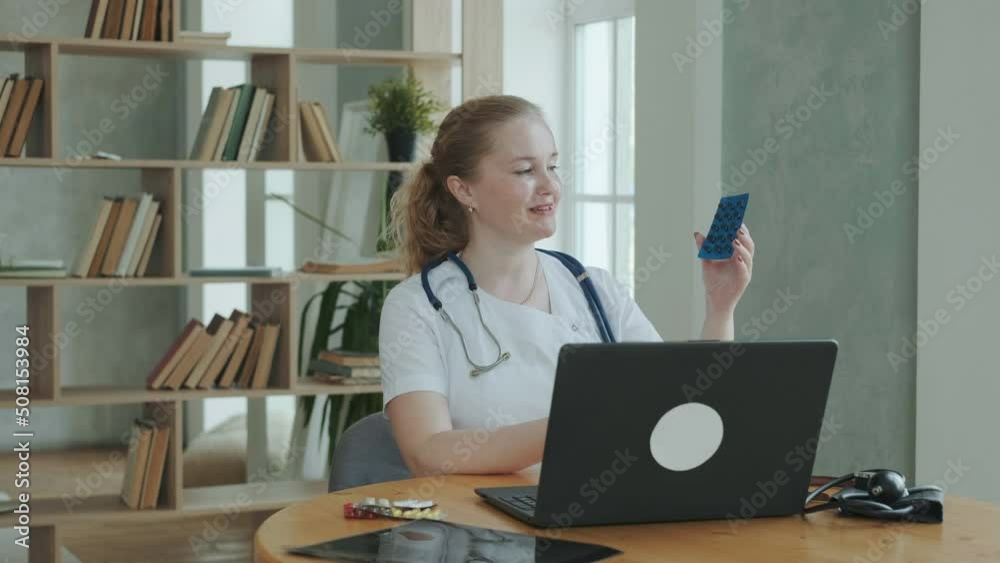 Professional doctor works at clinic. female therapist in overalls with stethoscope communicates via videoconference with patient and explains how to take prescription pills. Medical Care Online