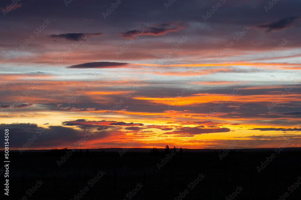 bright rich vibrant colourful sunset over silhouetted farm field 