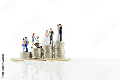 Financial dependency for family life or married life concept : Miniature figurine young couple on coins, depicting investment or savings money for future expense or obligations for a newly wed family.