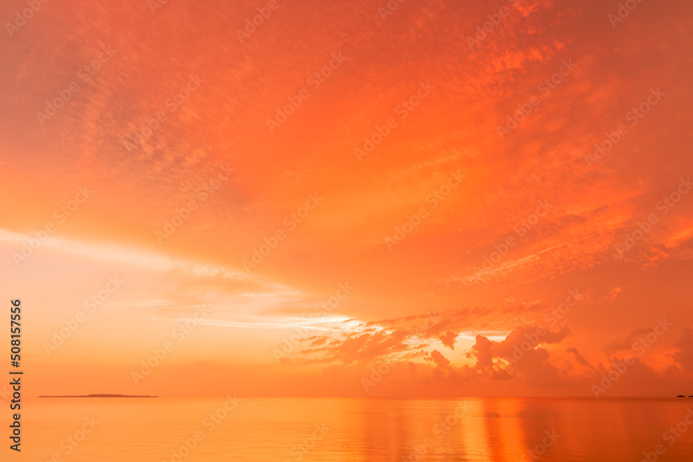 Amazing sunrise in orange shades at seashore, island on the horizon.