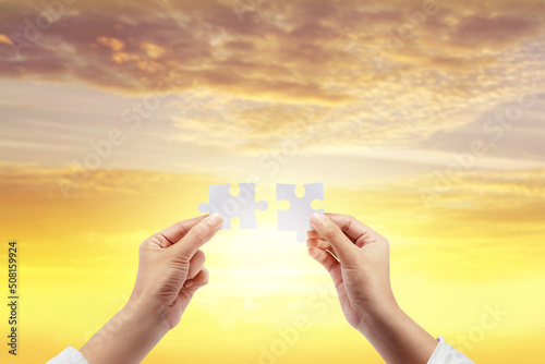 Two hands connect puzzle pieces against the sunset sky..Business teamwork concept idea.