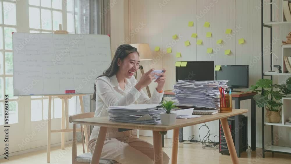 Asian Woman Enjoys Playing Game On Smartphone After Working With Documents At The Office
Asian Woman Enjoys Playing Game On Smartphone After Working With Documents At The Office