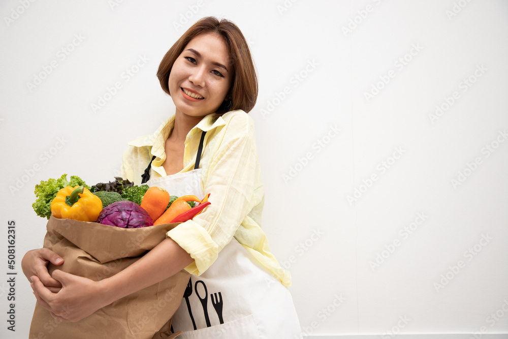 Cheerful caucasian Asian woman standing with shopping bag full of fresh fruits and vegetables in white room at home. Freshly bought vegetables Cheerful caucasian Asian woman standing with shopping bag full of fresh fruits and vegetables in white room at home. Freshly bought vegetables