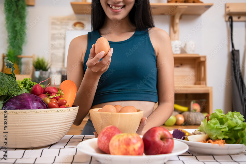 Young Asain beautiful woman holding fresh organic egg at home with surprise face in kitchen. Woman taking eggs and showing egg with happy face. Healthy homemade oatmeal