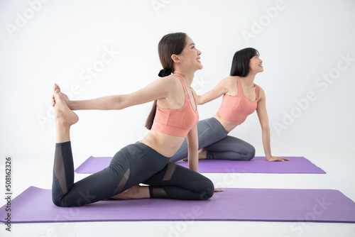 Pair of women doing yoga pose meditation in the white room. Healthy body posture with happy feeling in the morning. Sport and healthy concept.
