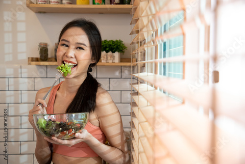 Sport girl dieting or good healthty concept. Young woman eating organic salad from vegetable in kitchen near cutain. Cooking young woman in kitchen with fork. Food blogger concept