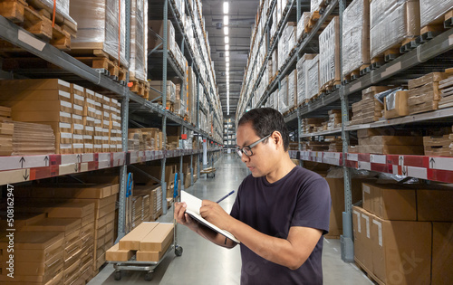 Warehouse worker writing on book. Distribution warehouse interior with shelve and boxes.