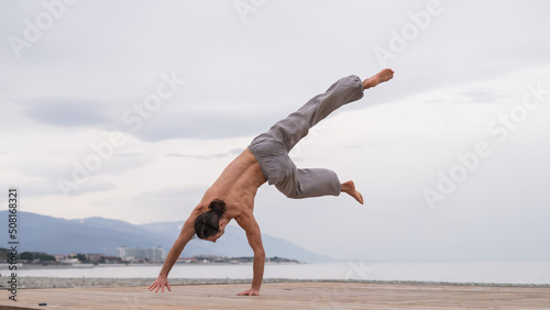 Shirtless caucasian man doing acrobatic wheel on the beach. 
