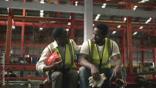 Tired worker man sit in warehouses worried taking break with friend from hard work thinking of production problems at factory, colleague encourage, engineering working in heavy industry factory