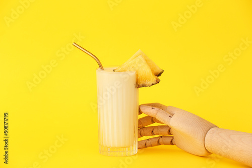 Wooden hand with glass of tasty cocktail on yellow background