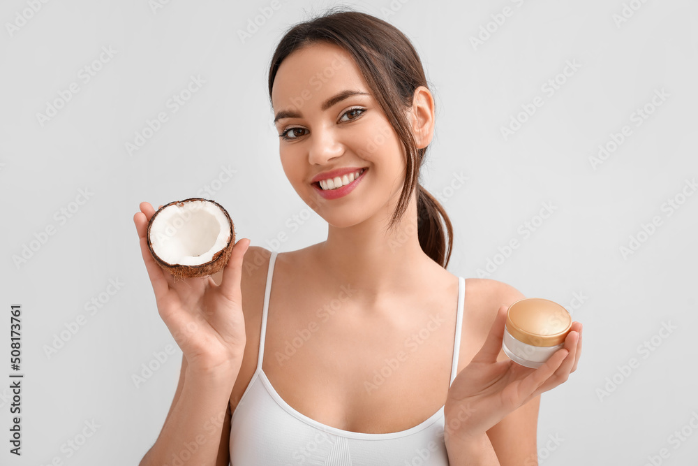 Young woman with coconut and jar of cream on light background Young woman with coconut and jar of cream on light background